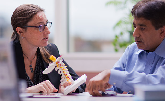 Photo of doctor showing 3D model of spine to a patient.