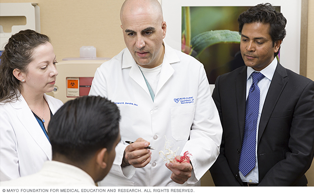 A neurosurgeon uses a 3D model of a person's brain tumor to explain the surgical plan.